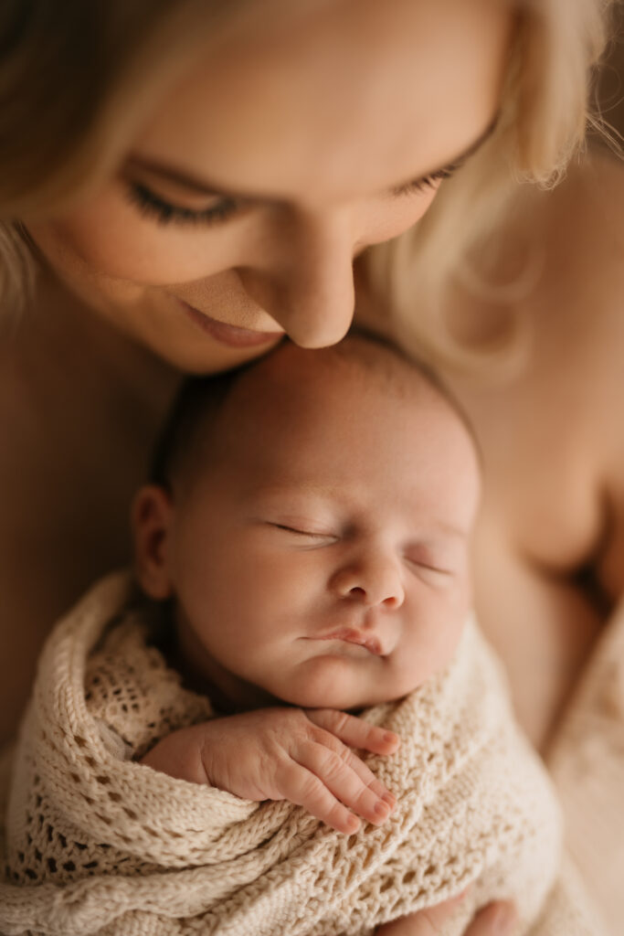 Photo of a newborn baby wrapped in a blanket and held by her mother demonstrating the style of natural newborn photography. 